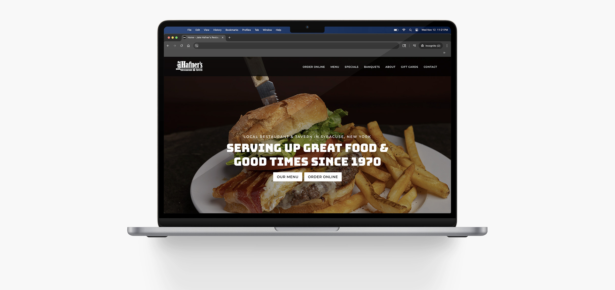 A laptop displaying a restaurant website with a background image of a sandwich, bacon, and fries. The screen reads: Serving up great food & good times since 1970 with buttons for the menu and online orders.